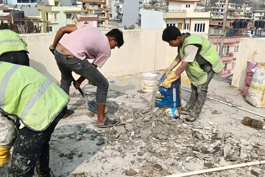 Workers preparing an old rooftop surface before waterproofing in Nepal